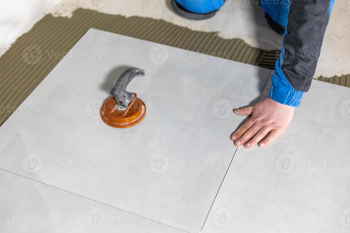 Tiler worker placing or tiling gray ceramic tile in the position over adhesive glue with lash tile leveling system, renovation or recontruction, concept of building photo