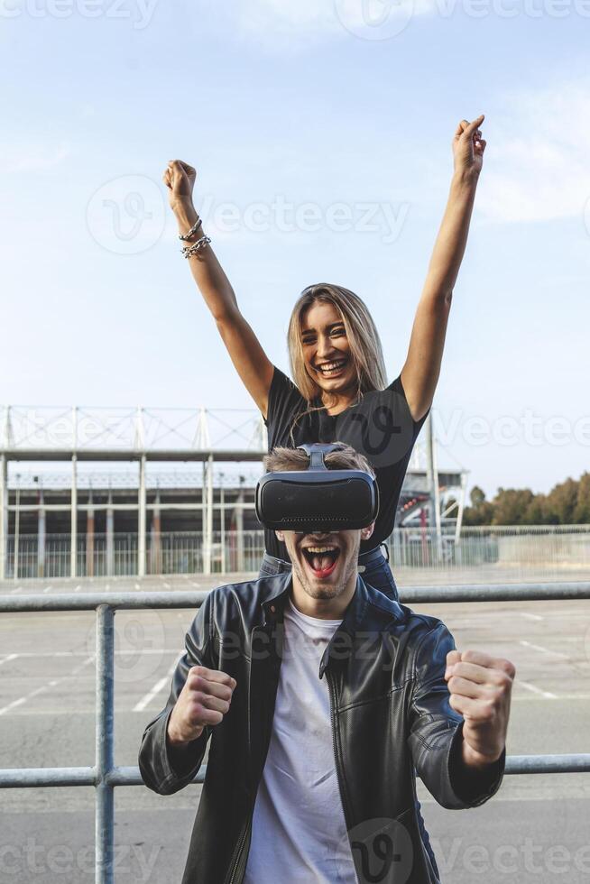 beautiful cheerful couple exulting in front of a stadium with virtual reality glasses photo