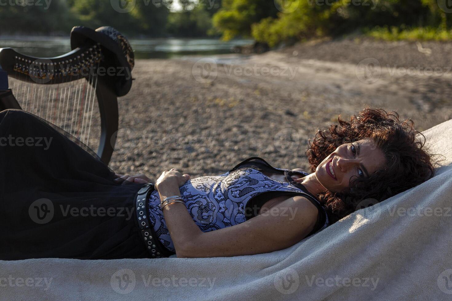 beautiful woman harp player relaxing on a beach along the river at sunset photo
