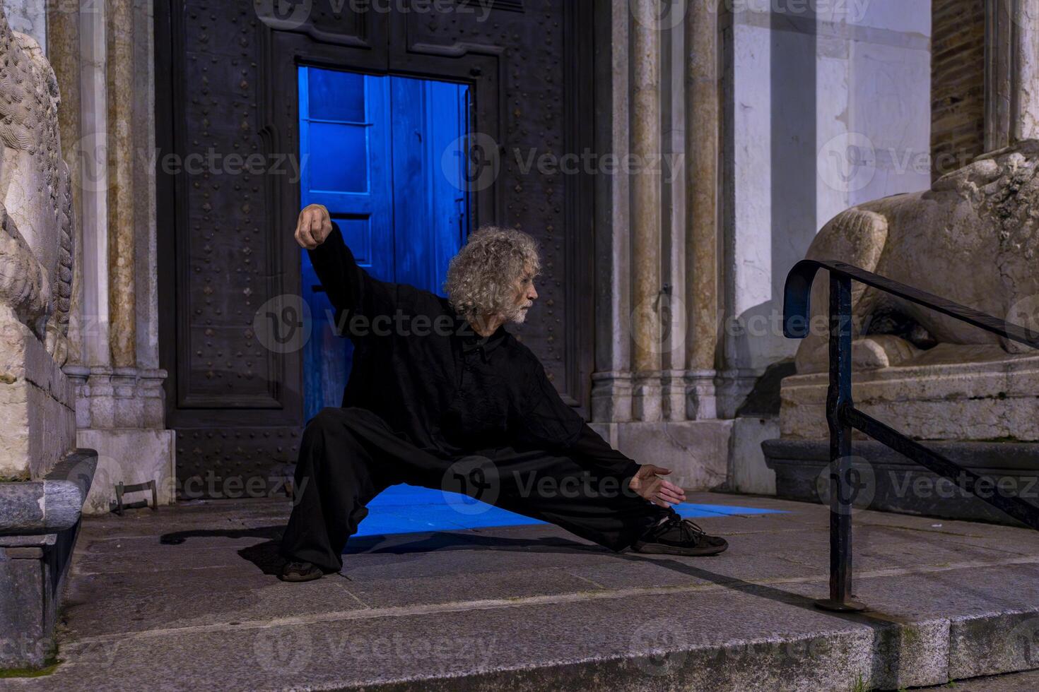 middle aged tai chi master showing stick exercises outdoors amidst the architecture of a medieval cathedral photo