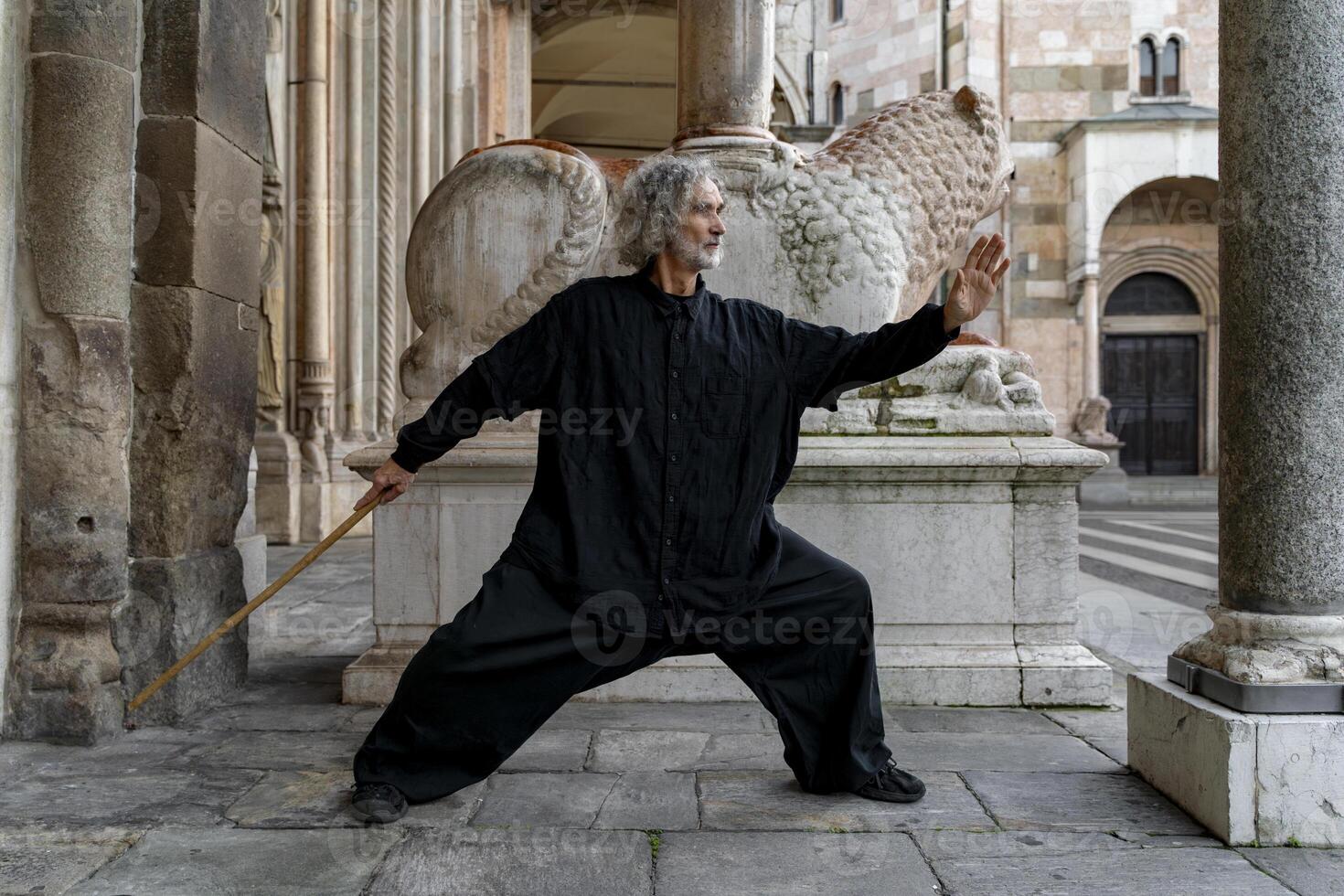 Middle-aged tai chi master showing stick exercises outdoors amidst the architecture of a medieval cathedral photo