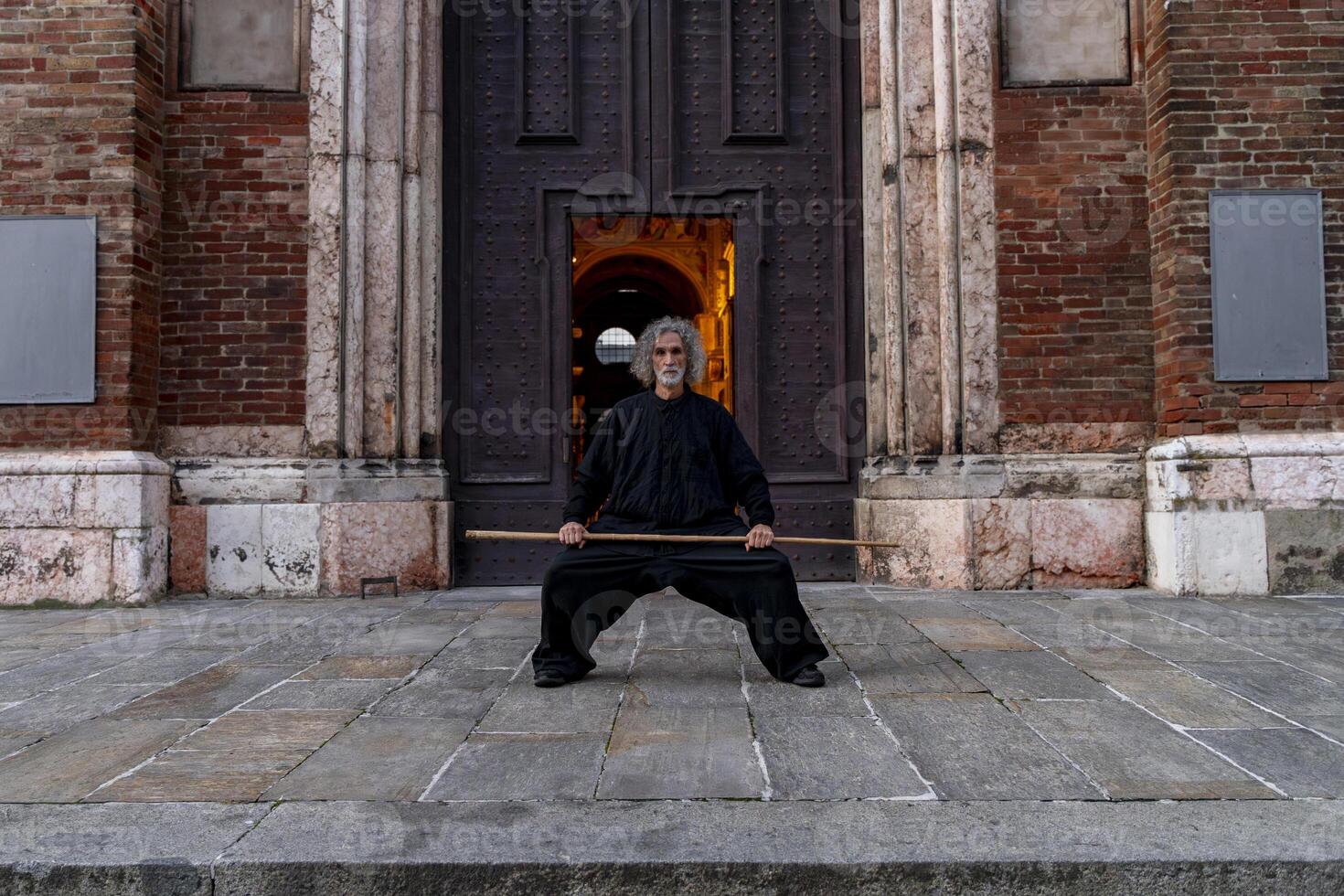 Middle-aged tai chi master showing stick exercises outdoors amidst the architecture of a medieval cathedral photo