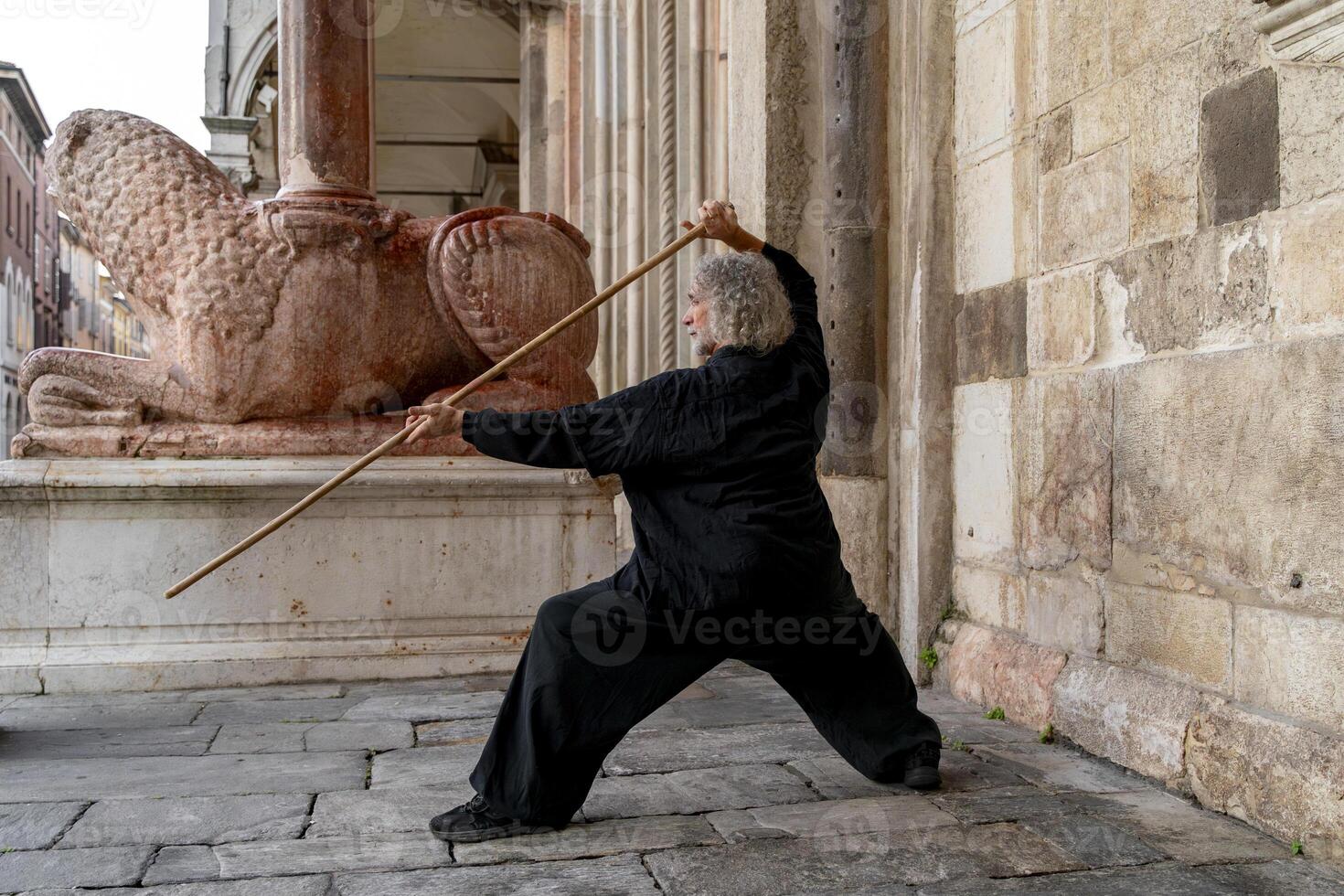 Middle-aged tai chi master showing stick exercises outdoors amidst the architecture of a medieval cathedral photo