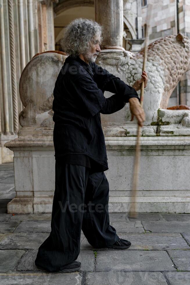 Middle-aged tai chi master showing stick exercises outdoors amidst the architecture of a medieval cathedral photo