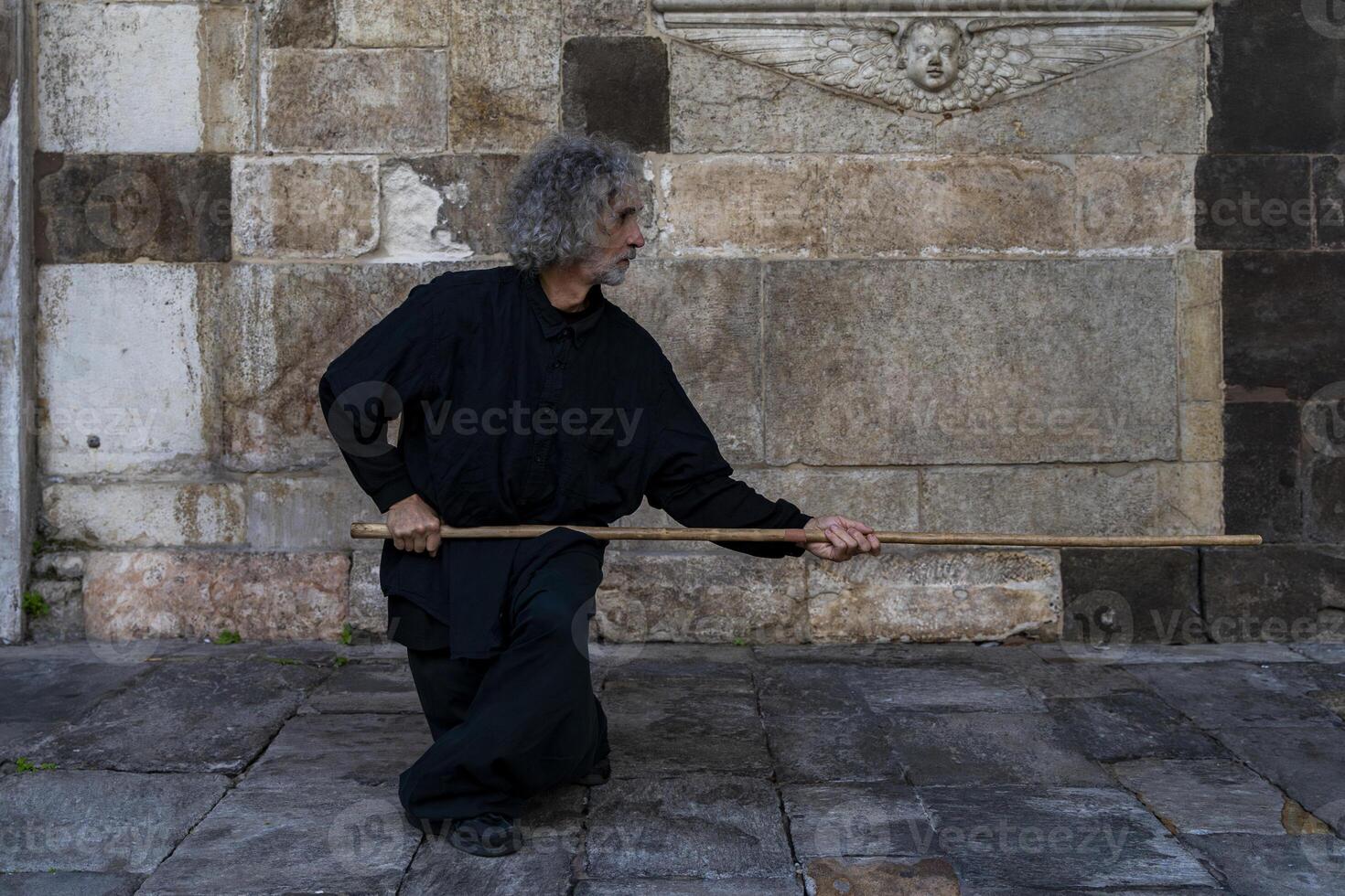 middle aged tai chi master showing stick exercises outdoors amidst the architecture of a medieval cathedral photo