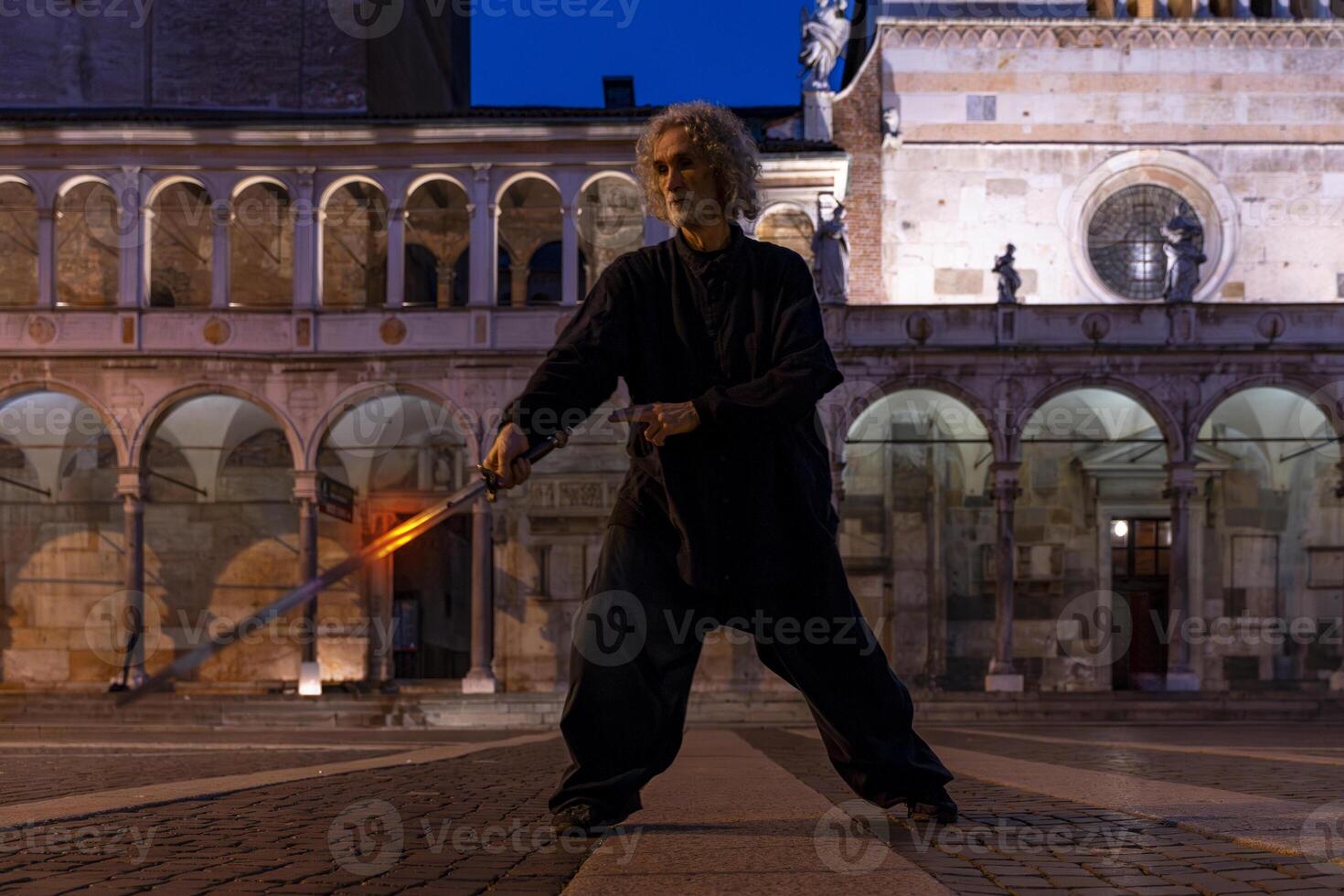 middle aged tai chi master showing stick exercises outdoors amidst the architecture of a medieval cathedral photo
