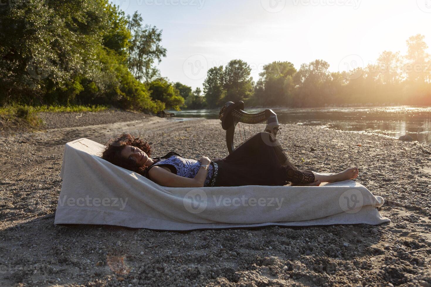 beautiful woman harp player relaxing on a beach along the river at sunset photo