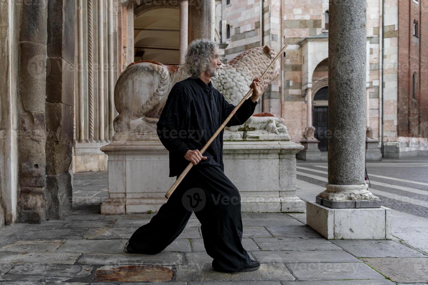 Middle-aged tai chi master showing stick exercises outdoors amidst the architecture of a medieval cathedral photo