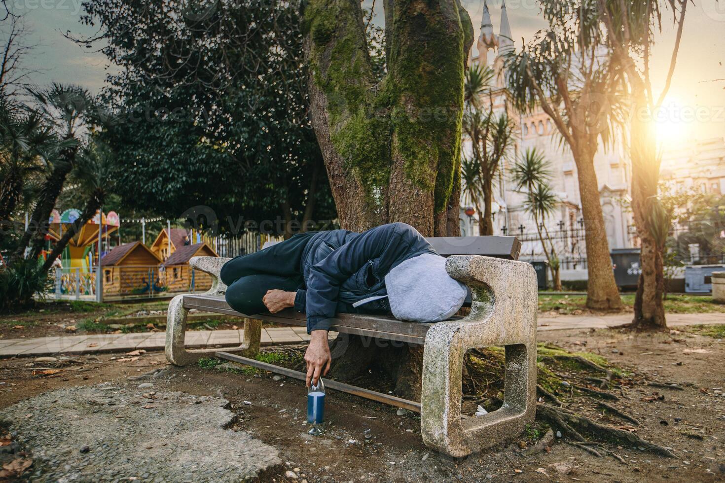 Homeless man or alcoholic sleeping on bench. Poor man on city street photo
