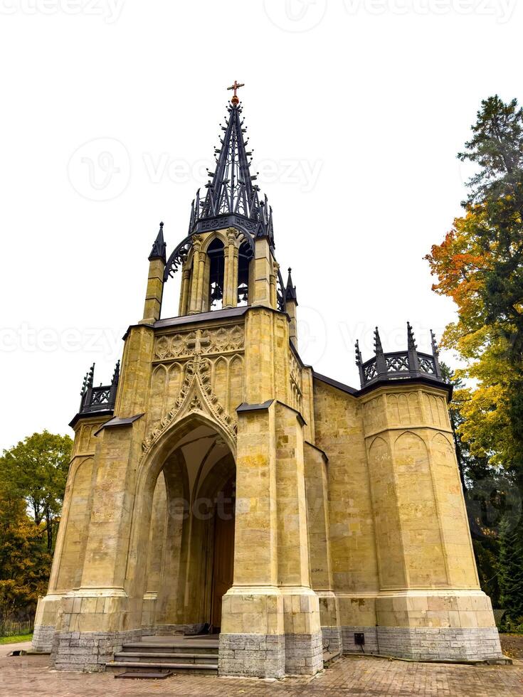 An imposing Gothic-style chapel with a tall, intricately detailed spire reaching into the overcast sky. The structure stands with its arched entrance and stone facade, embodying historical photo