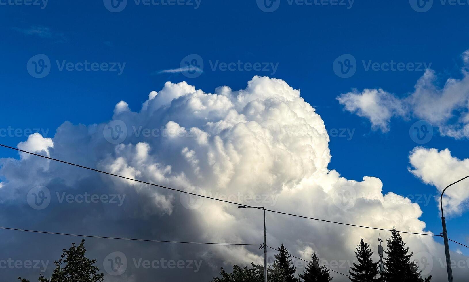 A breathtaking low-angle view capturing a towering cumulus cloud formation against a vivid blue sky. The sunlight enhances the cloud texture, highlighting the contrast between the bright white tops photo