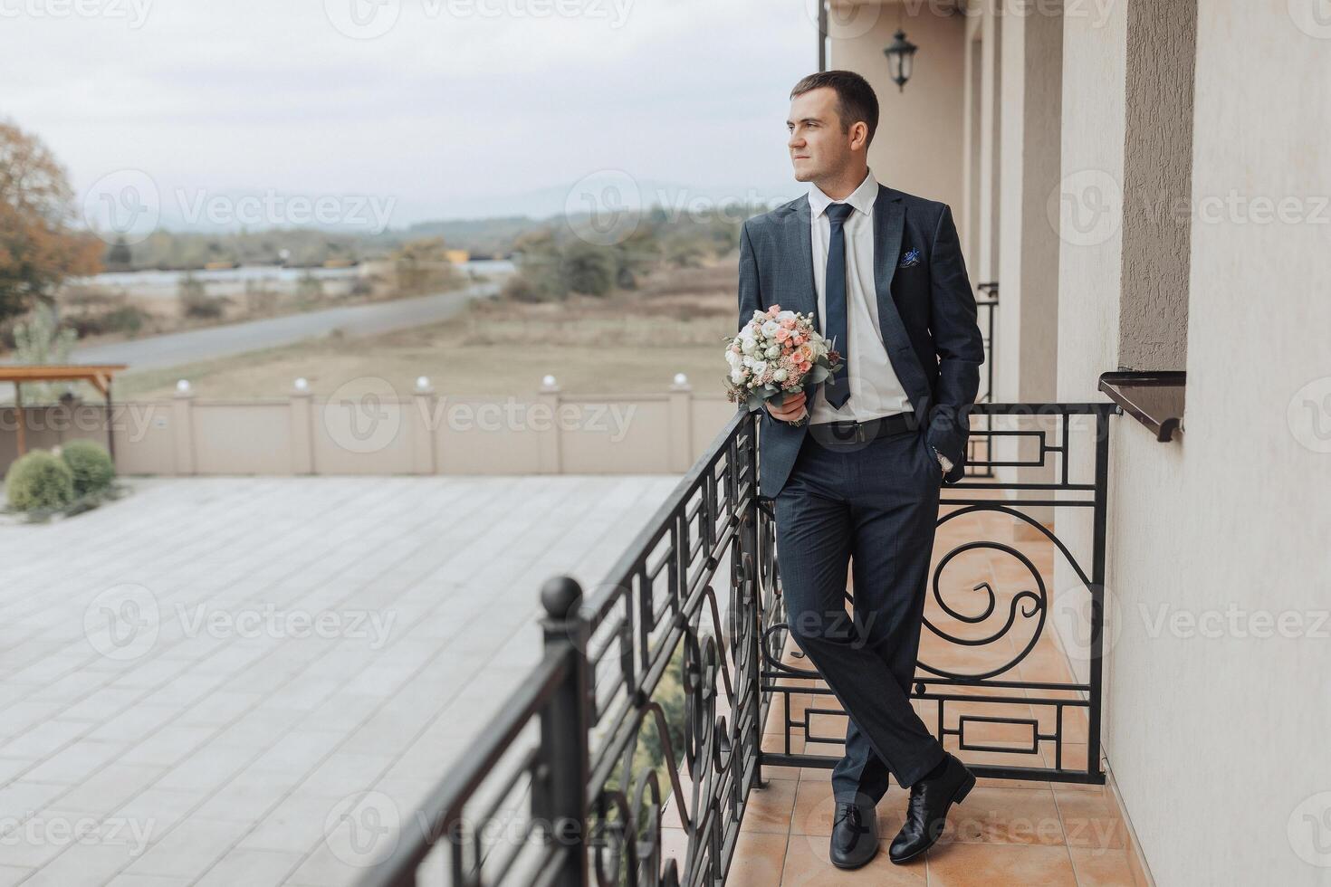 A man in a suit and tie stands on a balcony holding a bouquet of flowers photo