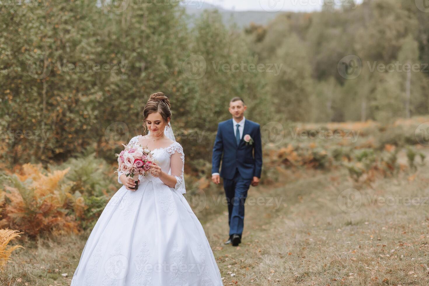A bride and groom are walking through a field with a bouquet and a tie photo