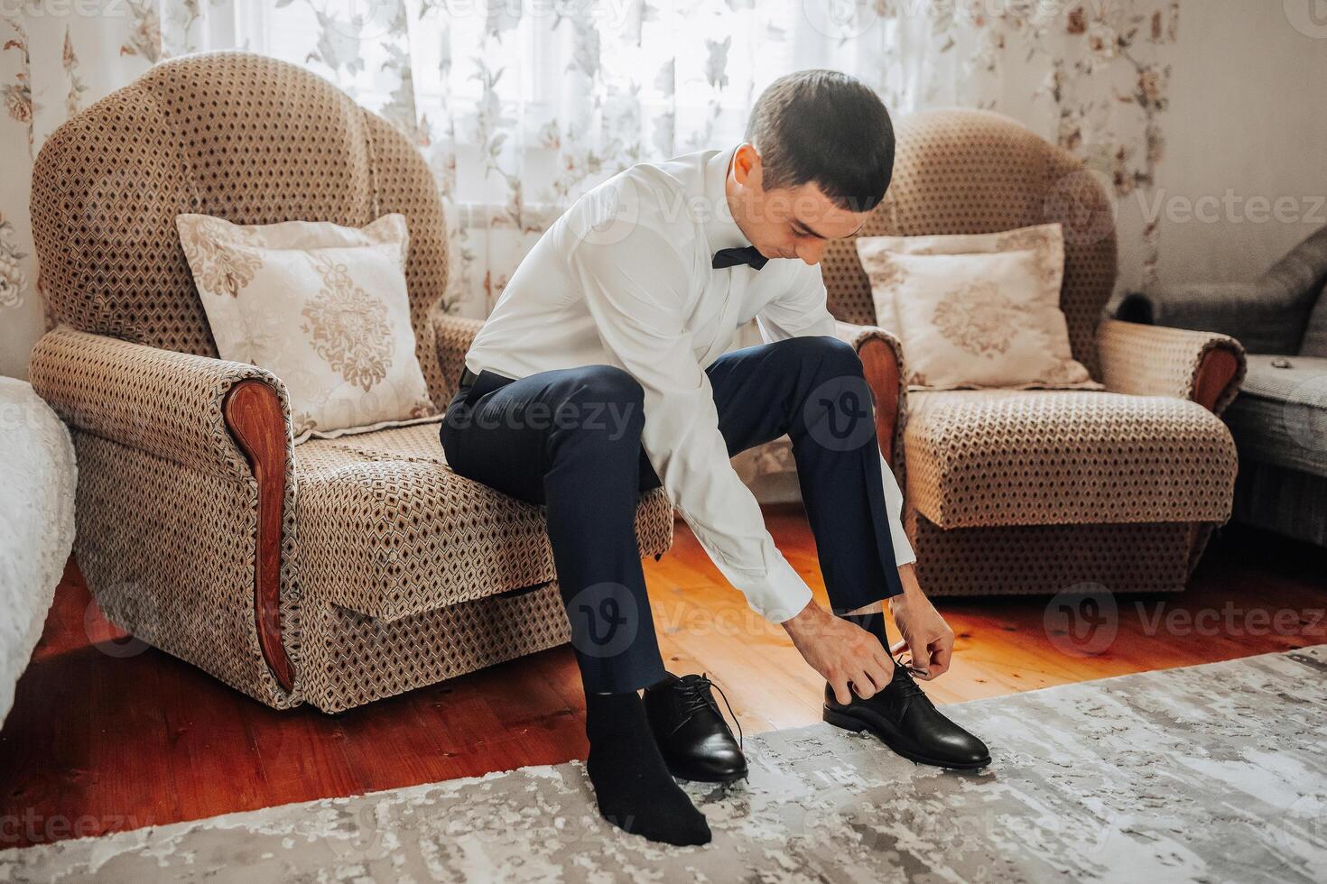 A man in a suit is sitting on a chair, putting on his shoes photo
