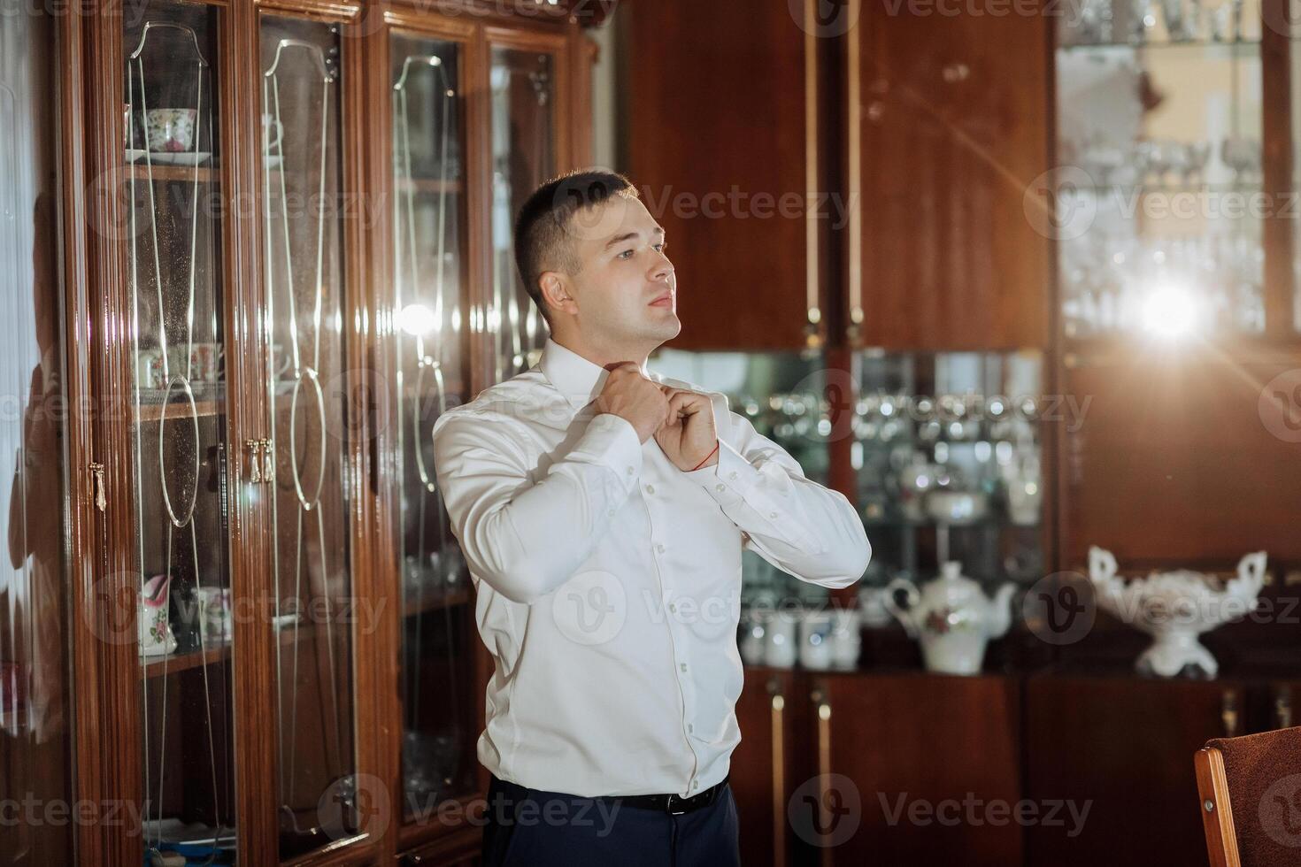A man in a white shirt is getting dressed in front of a cabinet photo