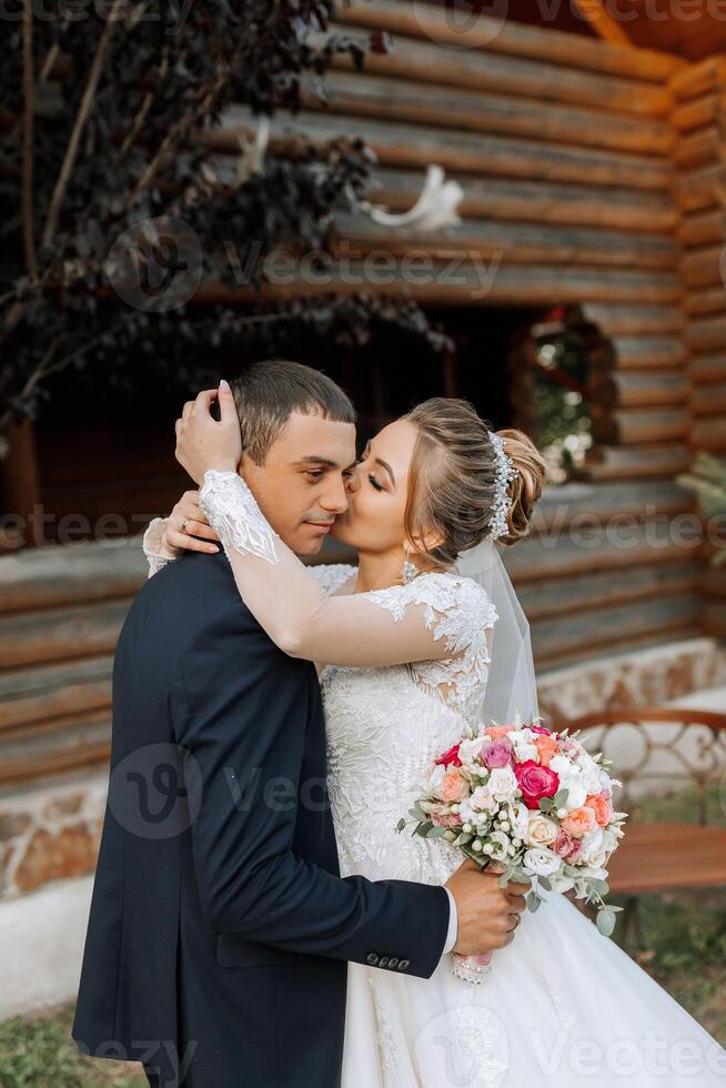 A bride and groom are hugging each other in front of a log cabin photo