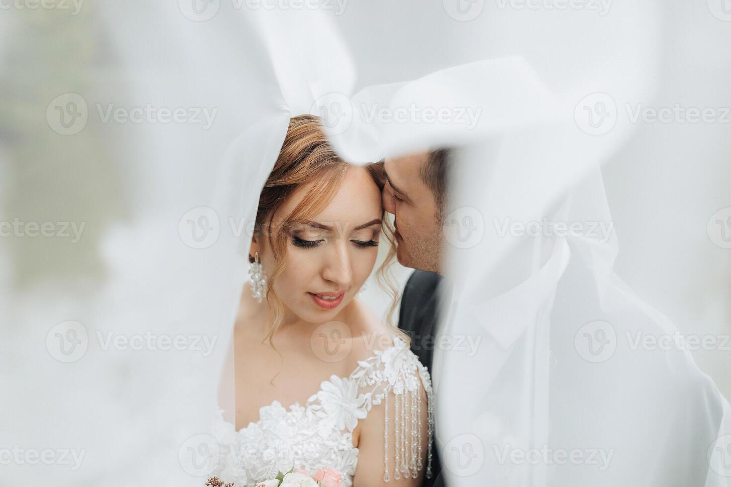 A bride and groom are kissing in front of a white curtain photo