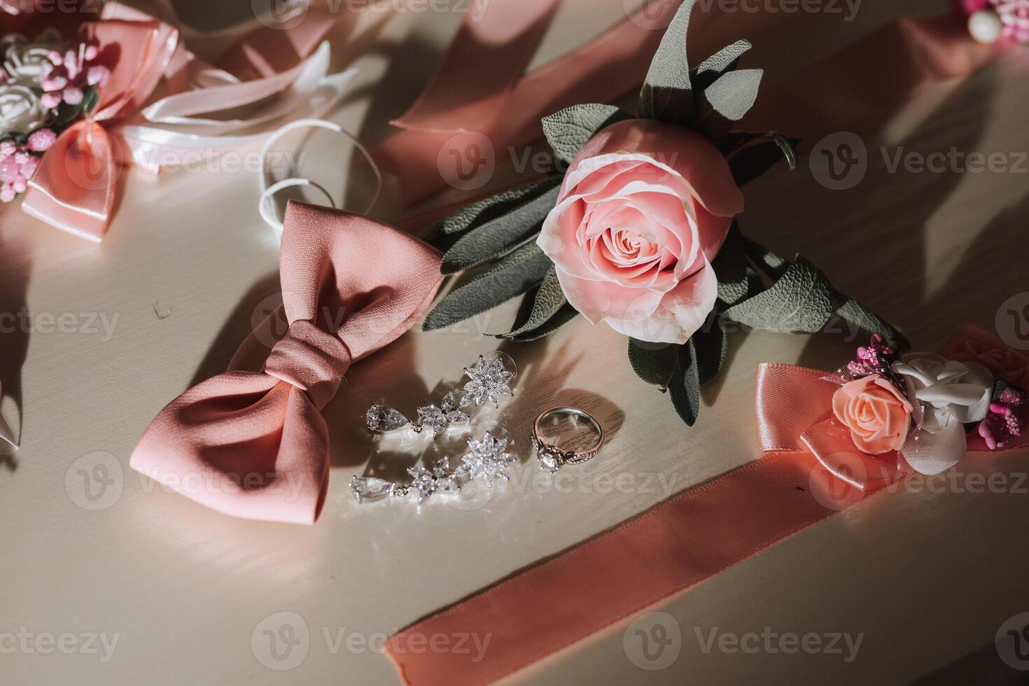 A pink rose is on a table with a pink bow and a ring photo