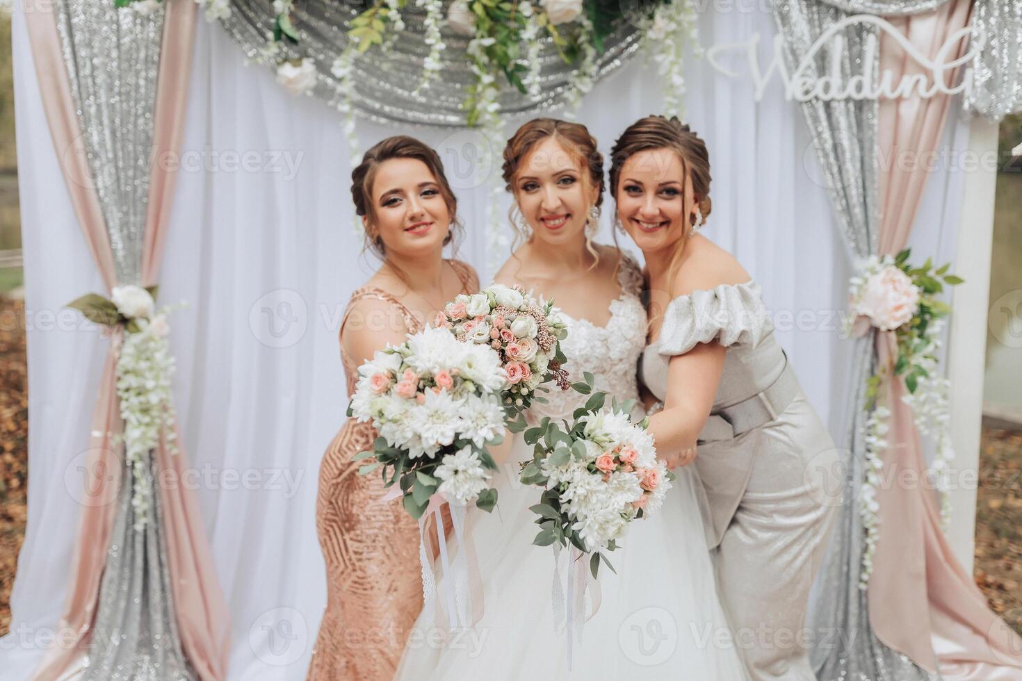 Three women posing for a photo in front of a wedding arch