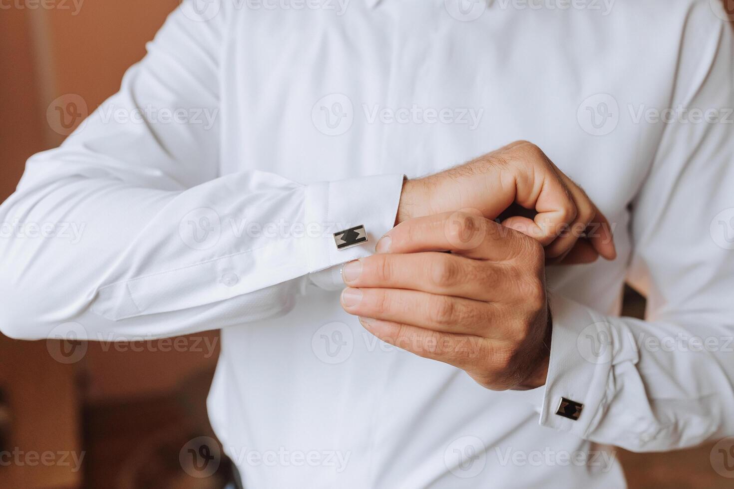 A man is getting ready to dress up in a white shirt and is adjusting his cuff photo