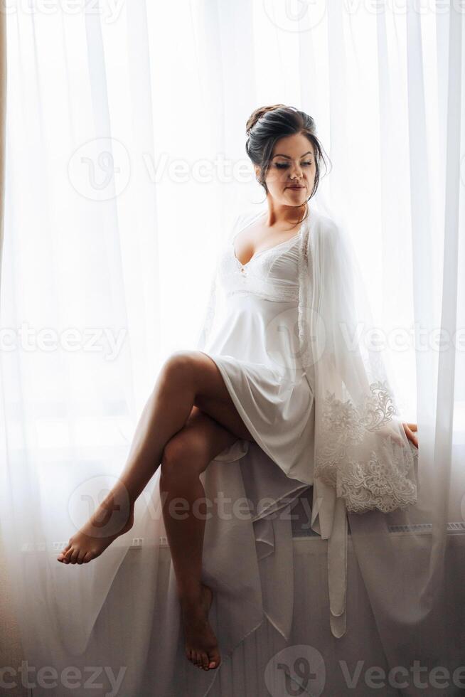A woman in a white dress sits in front of a window photo