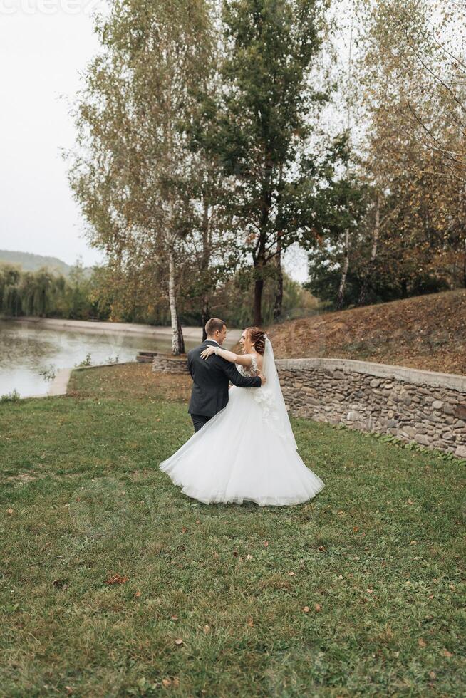 A bride and groom are dancing in a field near a body of water photo
