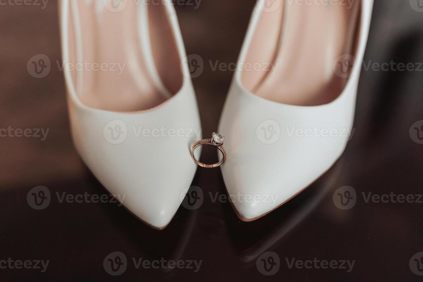 A pair of white shoes with a diamond ring on the left shoe photo