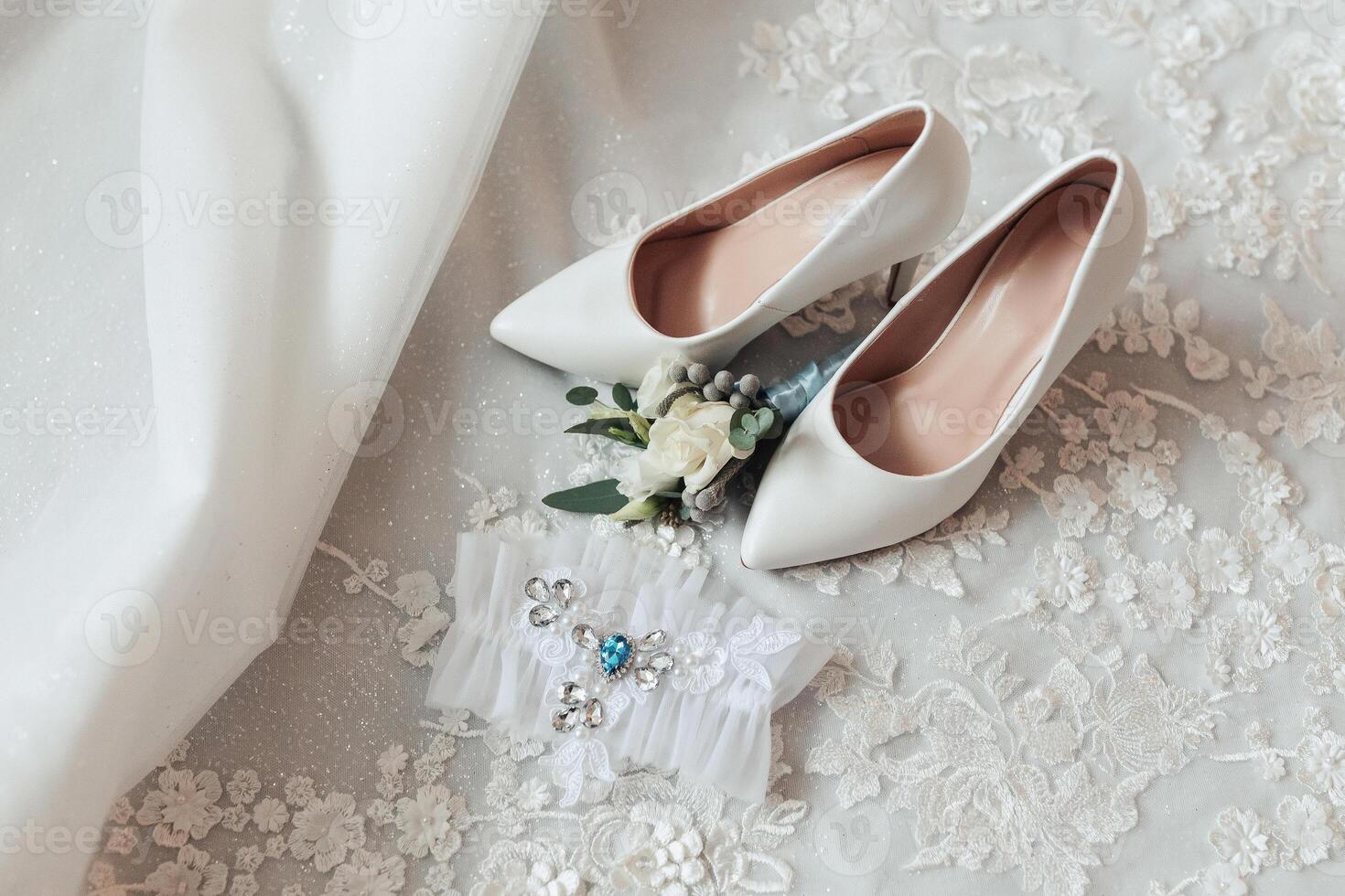 A pair of white shoes with a flower on them and a ring on the left foot photo