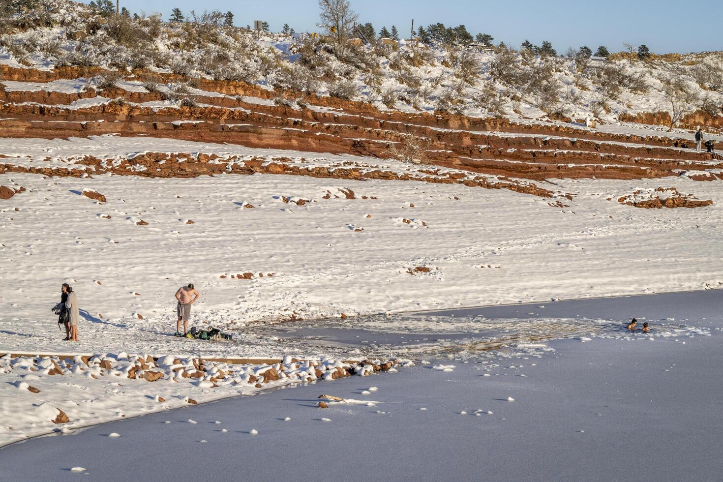 Fort Collins, CO, USA - February 4, 2024, Group of young people taking a cold water plunge in an ice hole in frozen Horsetooth Reservoir at Colorado foothills. photo