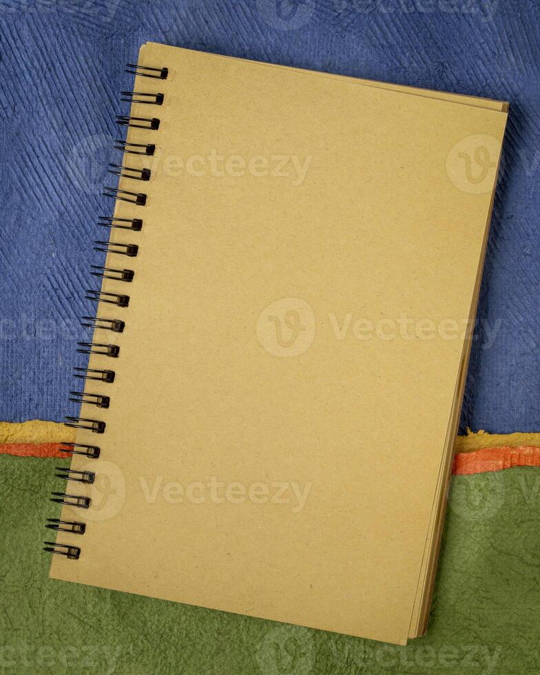 blank spiral notebook against abstract paper landscape, vertical poster photo