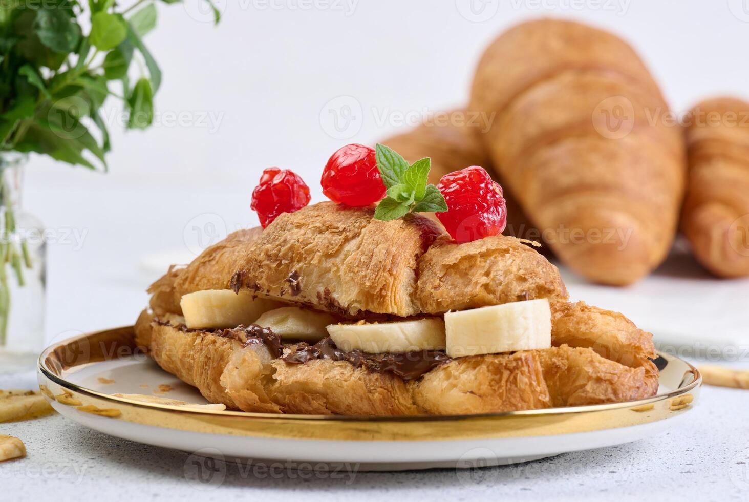 Croissant with banana pieces, chocolate paste in a round white plate photo