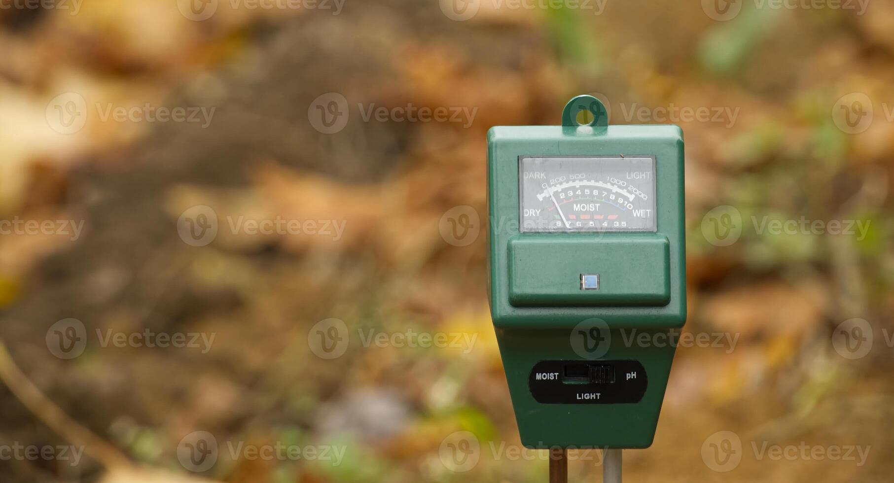 Soil moisture meter in garden monitors moisture level amidst autumn leaves and soil photo