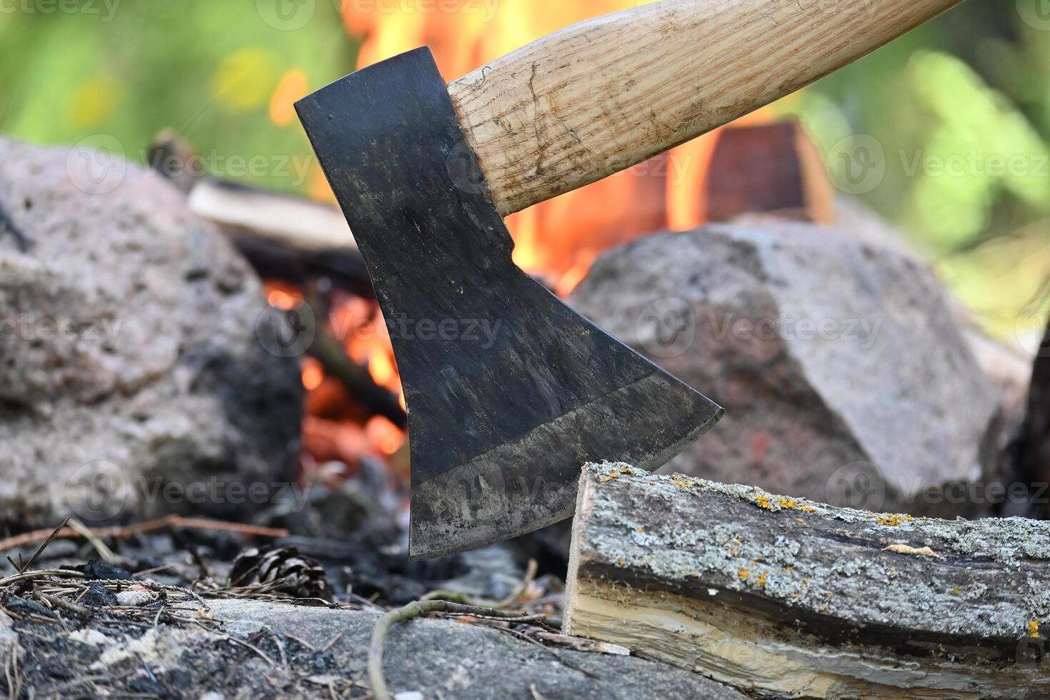 Hatchet lodged in a log of wood, situated opposite a campfire photo