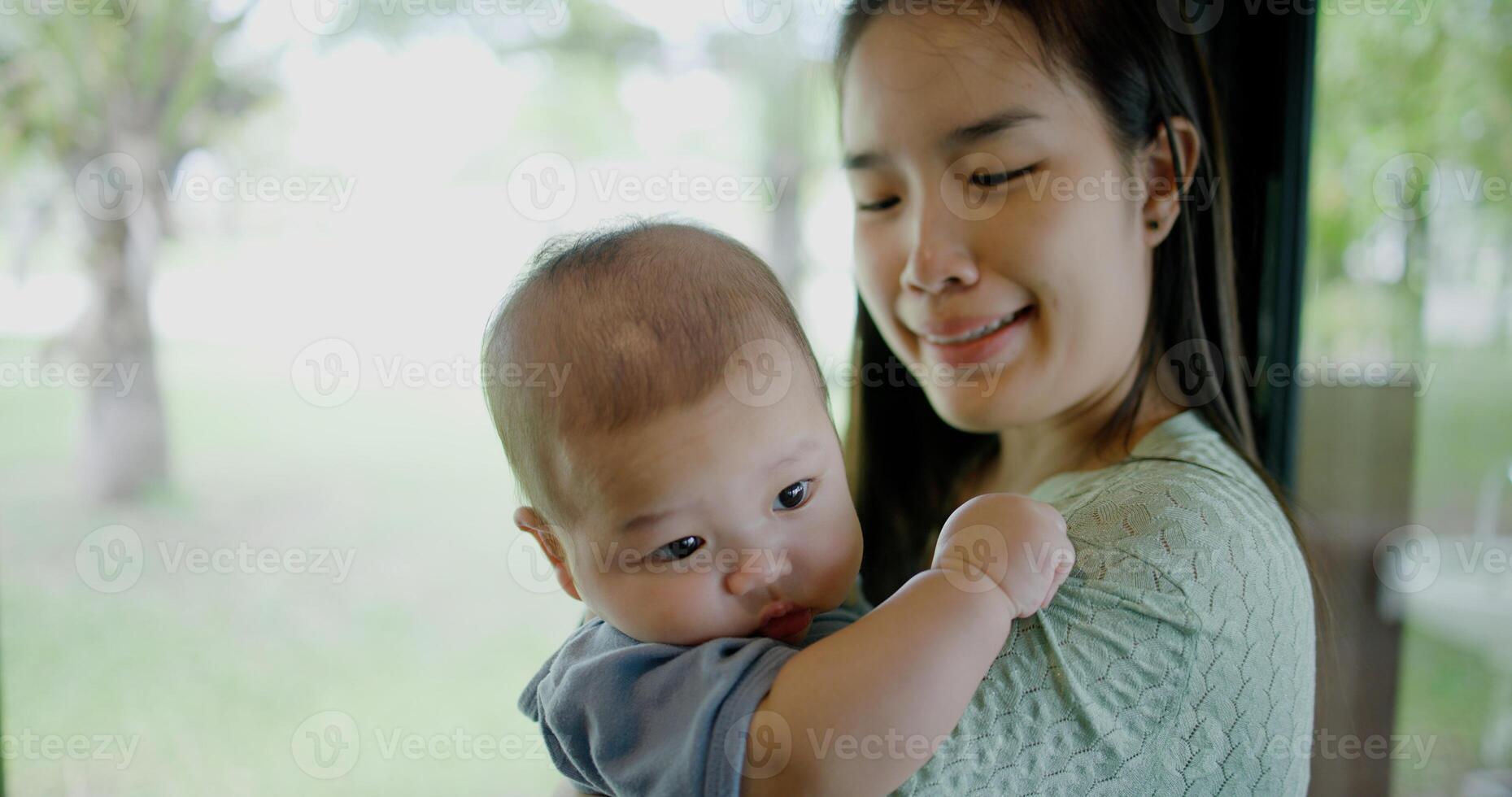 Portrait of Beautiful woman stands in a coffee shop, smiling warmly as she gently cradles a baby boy in her arms. Relaxed atmosphere add to the heartwarming moment. photo