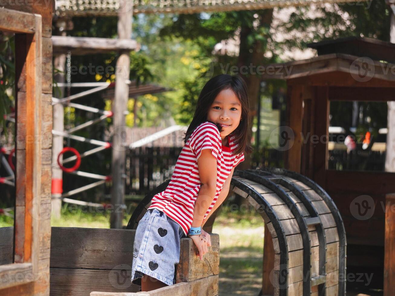Children play outdoors on a wooden playground in a park. Happy girl playing with wooden train in playground during summer. photo