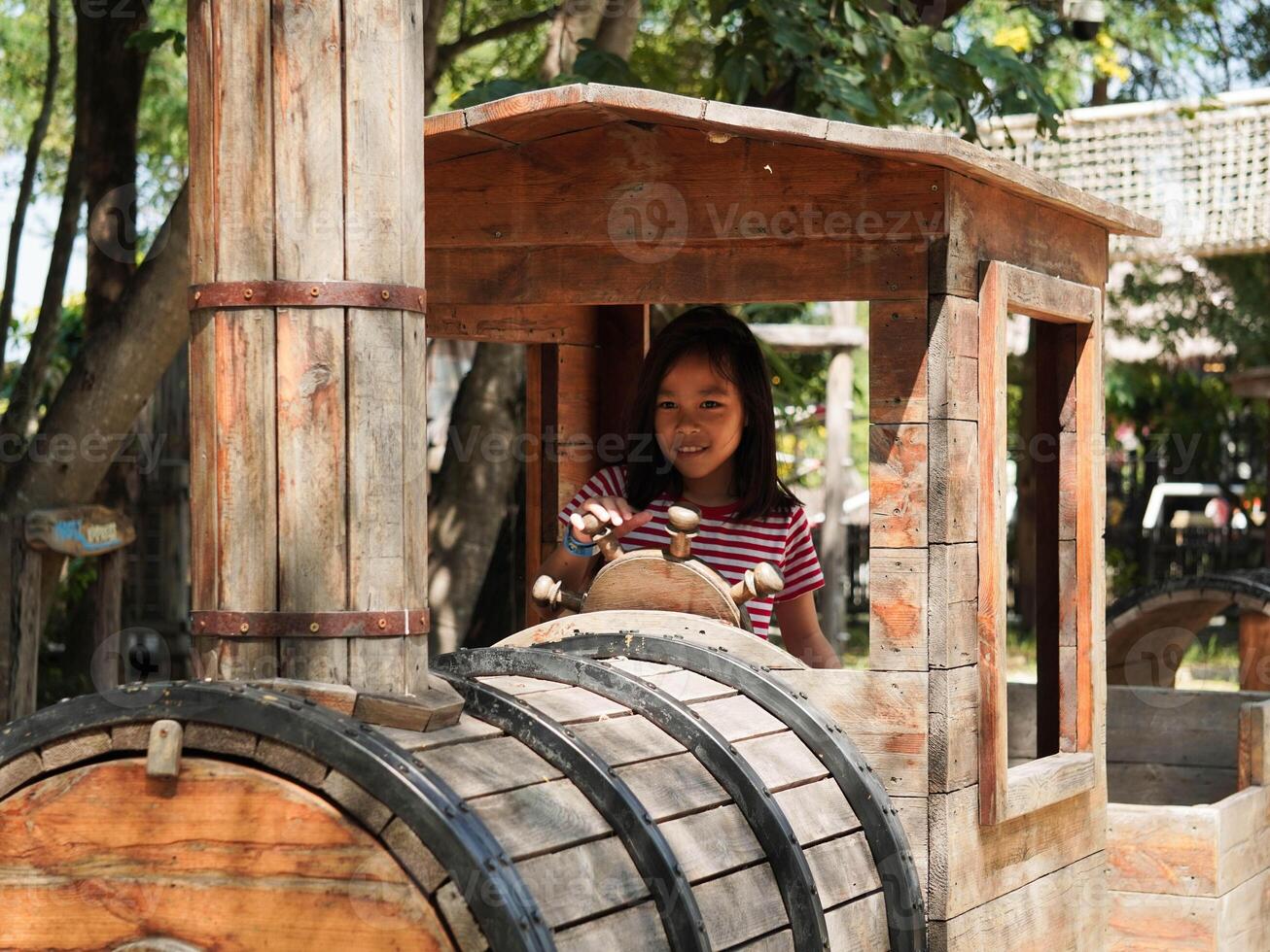 Children play outdoors on a wooden playground in a park. Happy girl playing with wooden train in playground during summer. photo