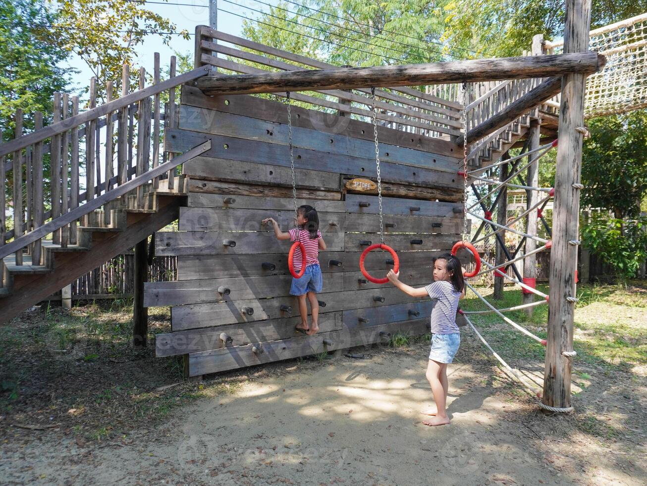 Children play outdoors on a wooden playground in a park. Happy girl playing on climbing swings in playground during summer. photo