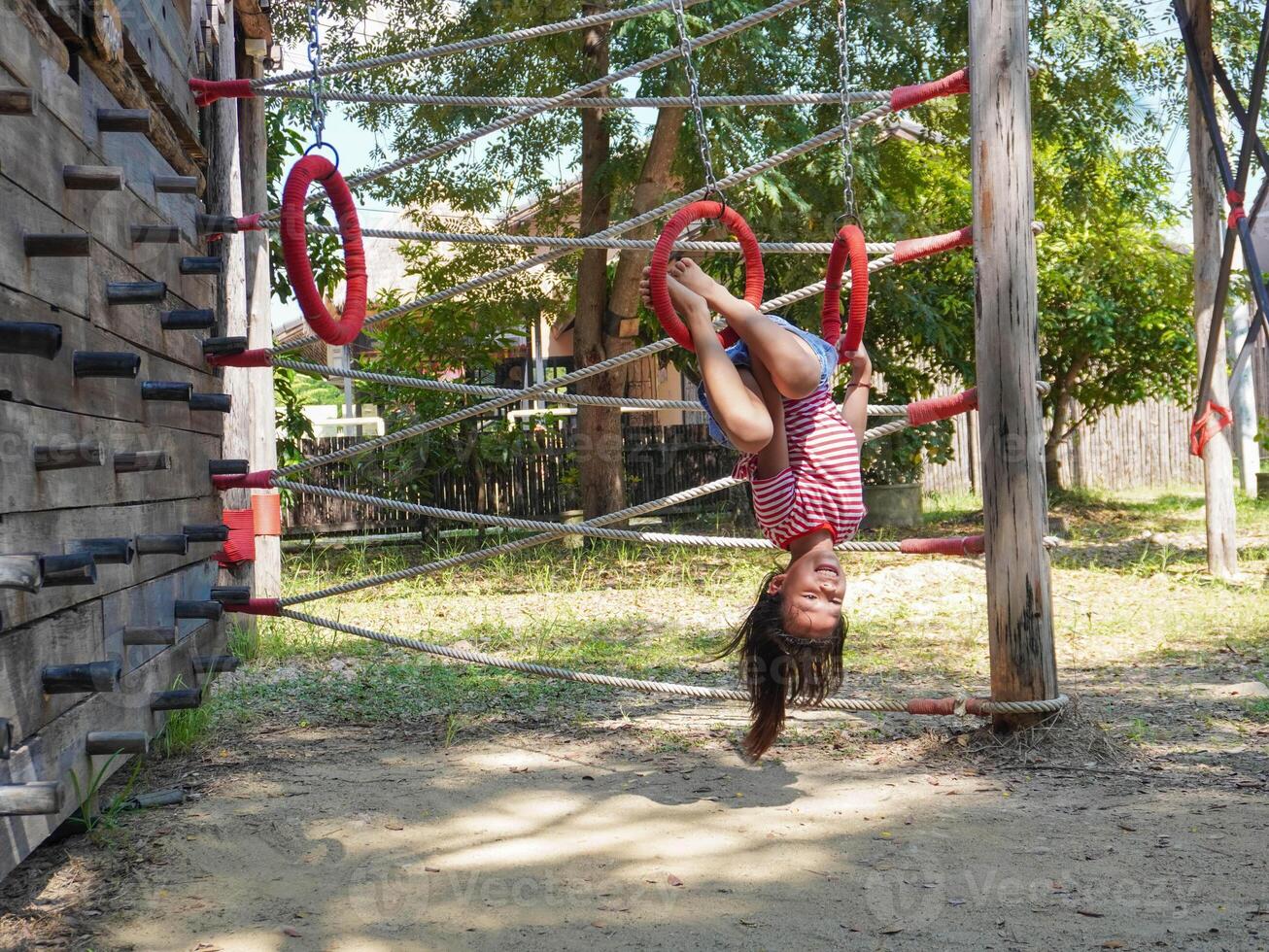 Children play outdoors on a wooden playground in a park. Happy girl playing on climbing swings in playground during summer. photo