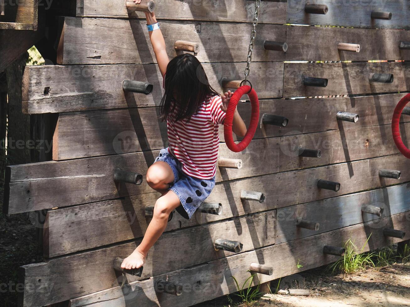 Children play outdoors on a wooden playground in a park. Happy girl playing on wooden climbing wall in playground during summer. photo