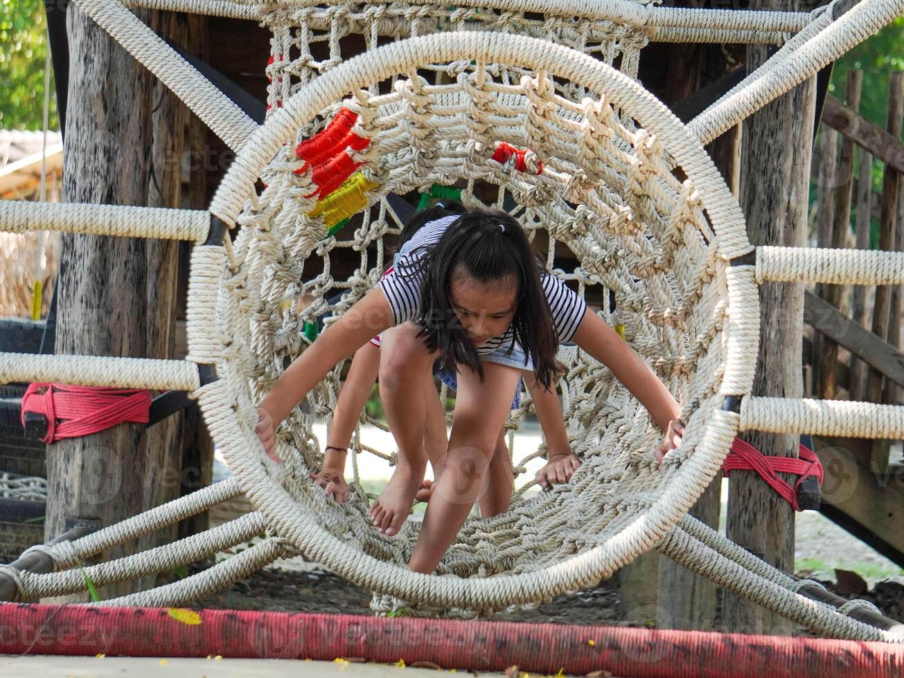 Children play outdoors on a wooden playground in a park. Happy girl playing on a rope net bridge in playground during summer. photo