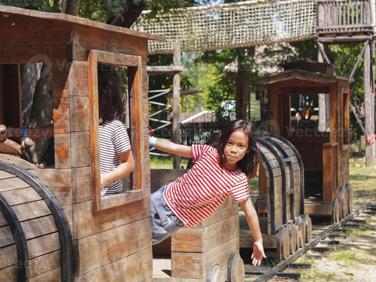 Children play outdoors on a wooden playground in a park. Happy girl playing with wooden train in playground during summer. photo