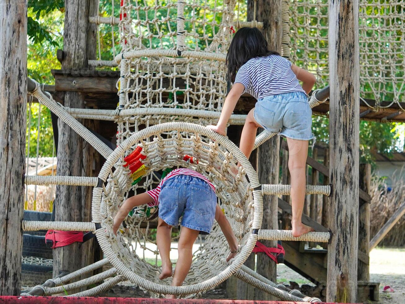 Children play outdoors on a wooden playground in a park. Happy girl playing on a rope net bridge in playground during summer. photo