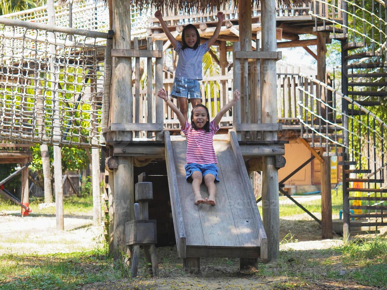 Children play outdoors on a wooden playground in a park. Happy girl playing on slide in playground in summer. photo