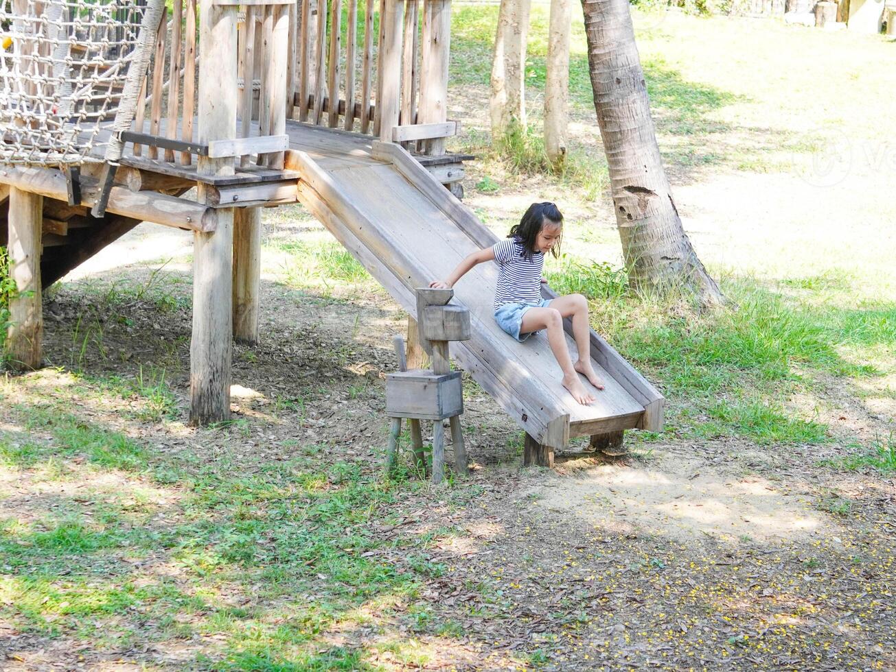 Children play outdoors on a wooden playground in a park. Happy girl playing on slide in playground in summer. photo