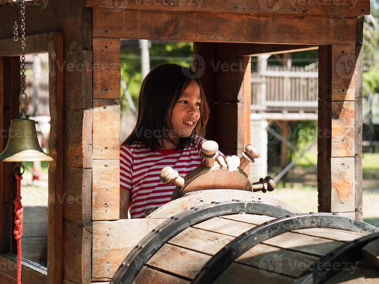 Children play outdoors on a wooden playground in a park. Happy girl playing with wooden train in playground during summer. photo