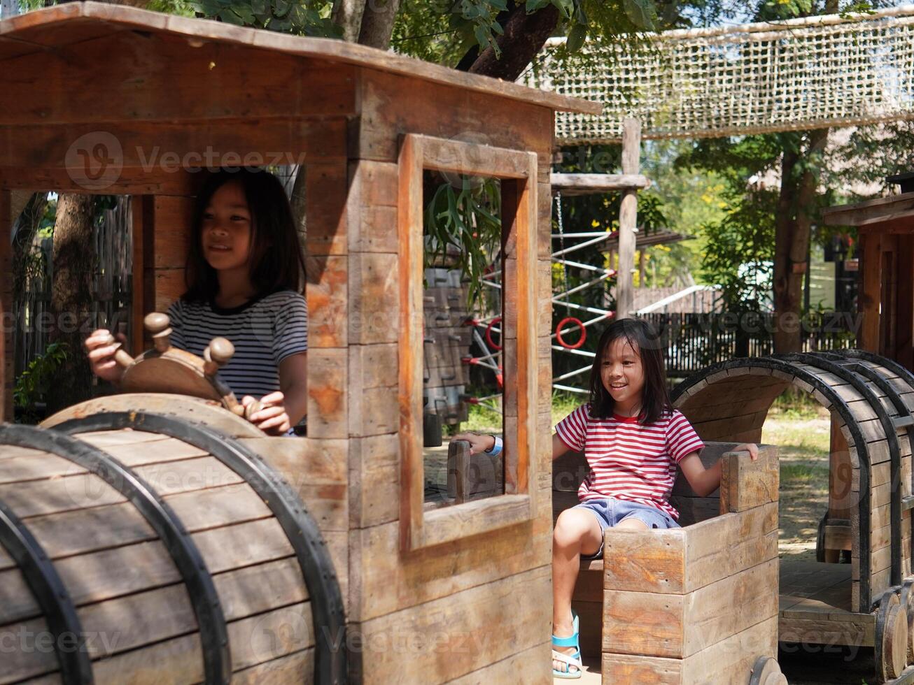 Children play outdoors on a wooden playground in a park. Happy girl playing with wooden train in playground during summer. photo