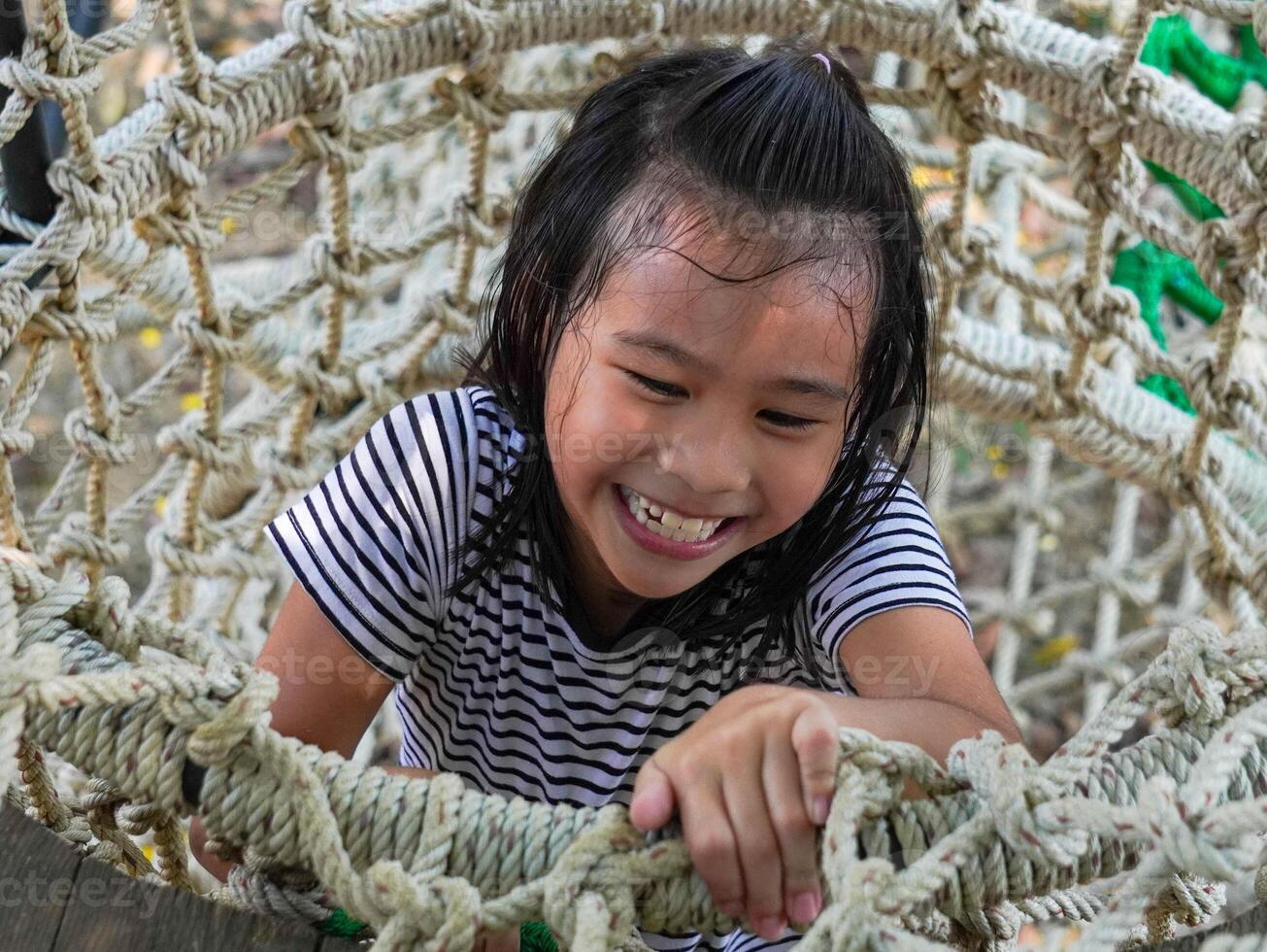 Children play outdoors on a wooden playground in a park. Happy girl playing on a rope net bridge in playground during summer. photo
