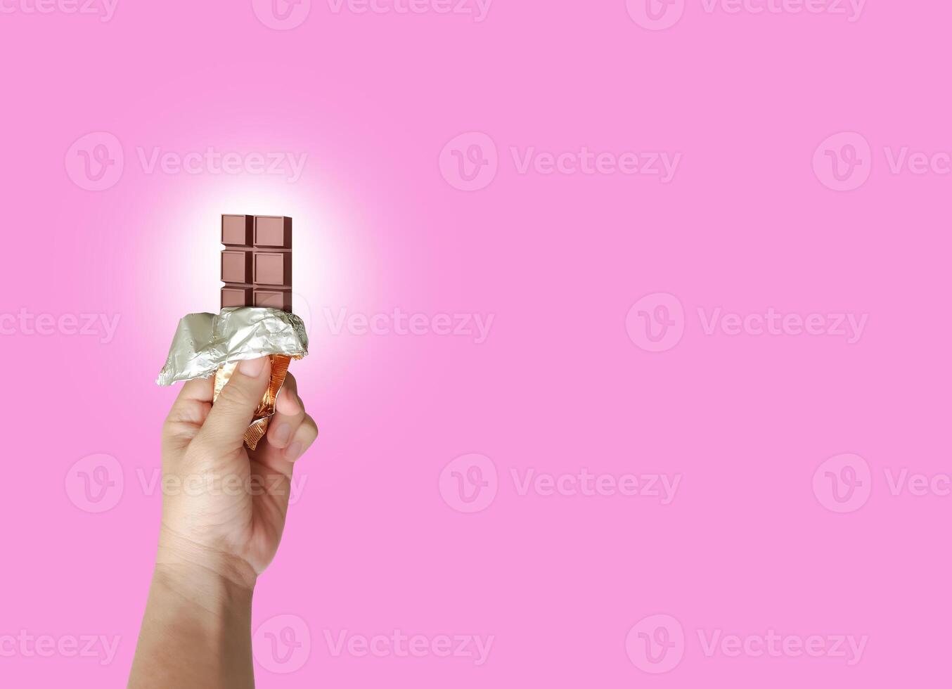 In hand is brown chocolate on pink background. Sweets in opened package. photo