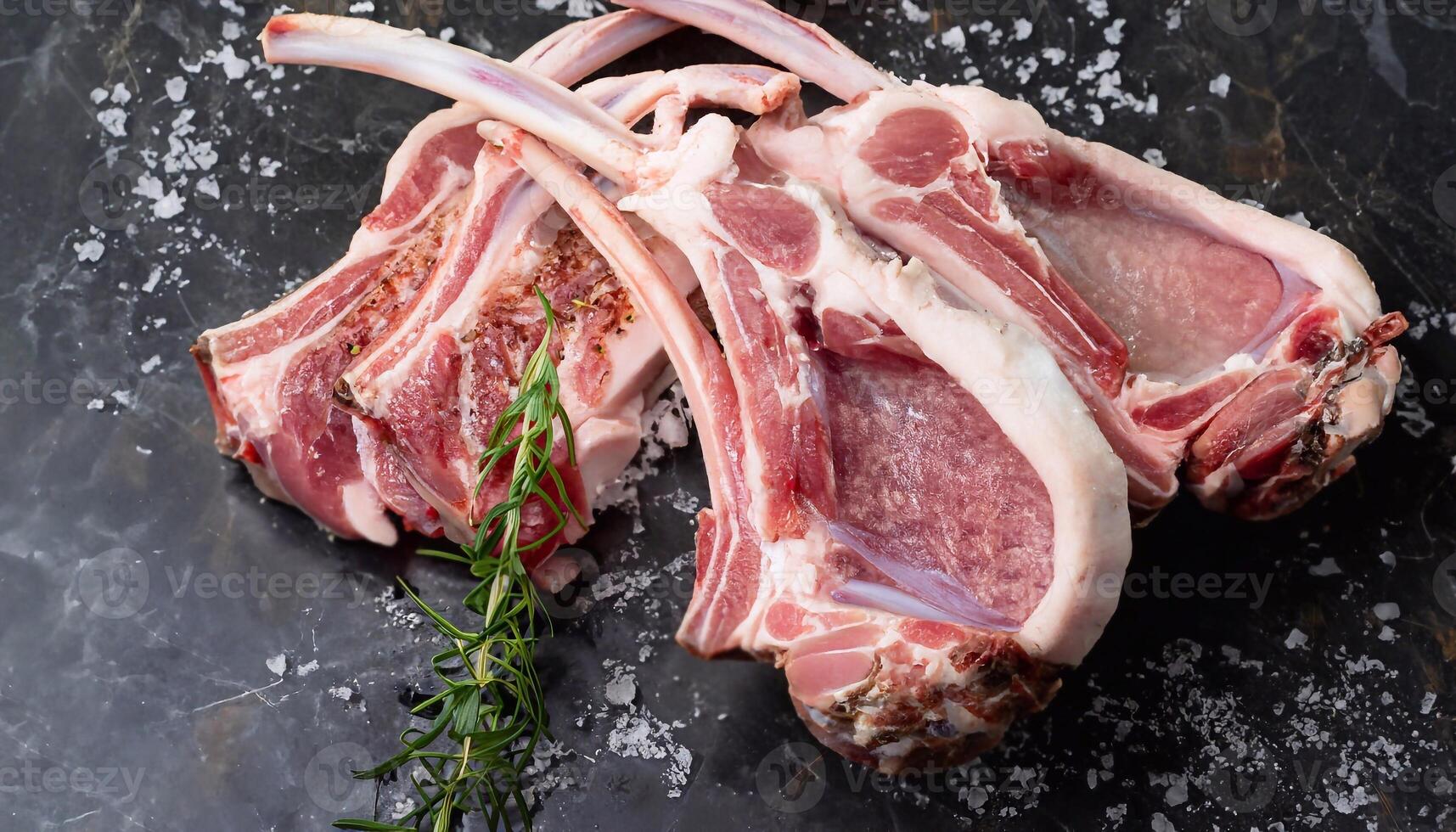 macro photo of sliced lamb carcass on black marble with sea salt crumbs and rosemary sprig