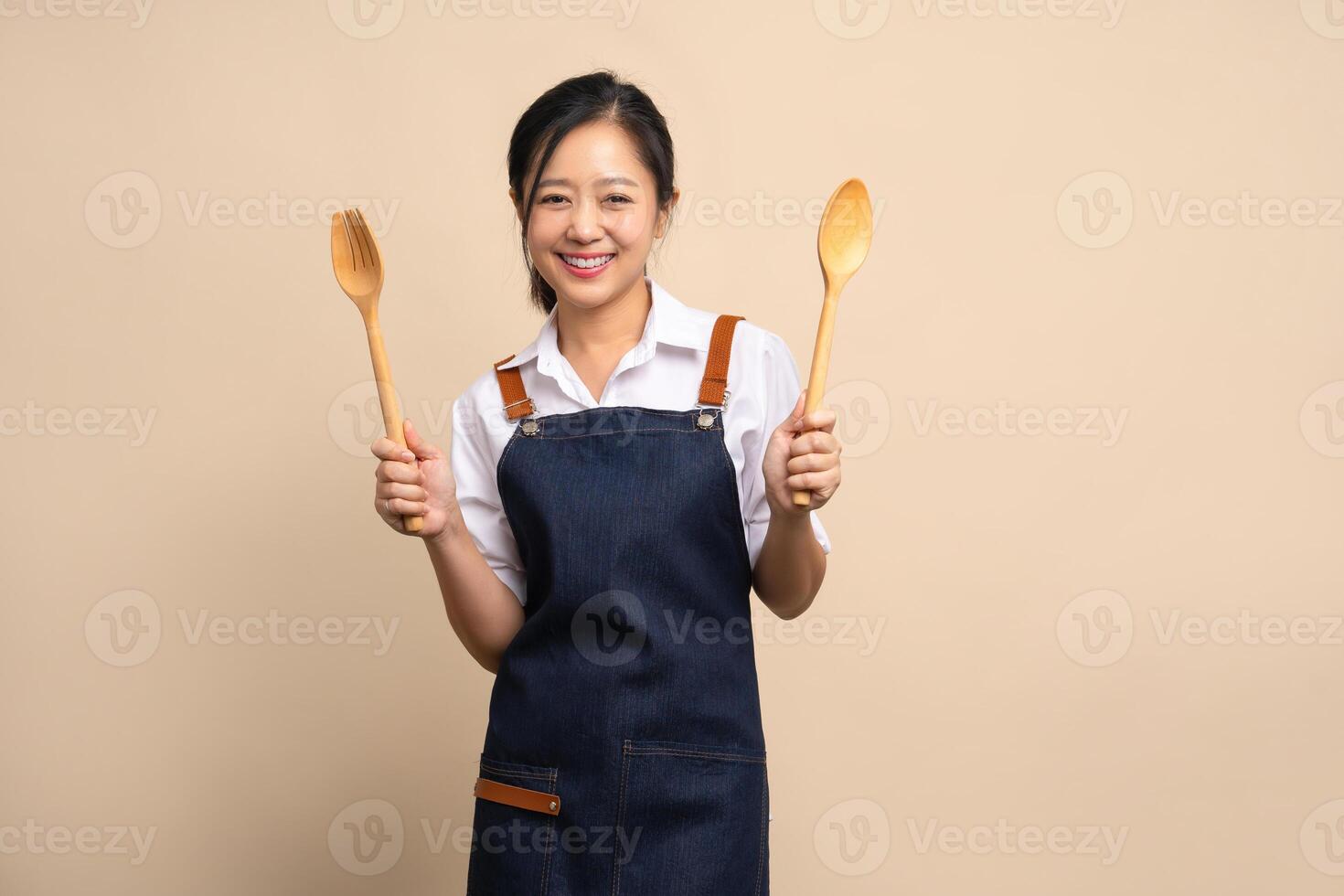 Portrait of young Asian woman in apron on beige background. Cooking and entrepreneurship concept. photo